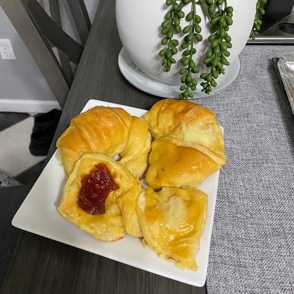 A white plate holds golden Argentinian pastries, some filled with guava paste, others with cheese.