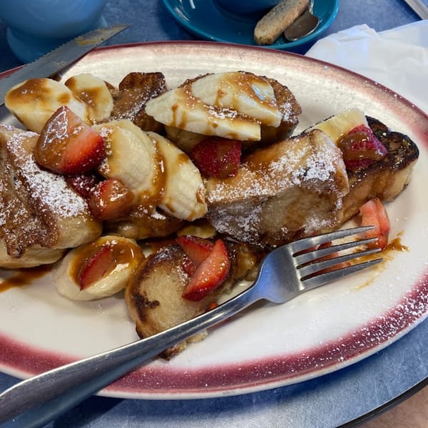Patria Station Café's French toast with bananas, strawberries, caramel, and powdered sugar on a plate.