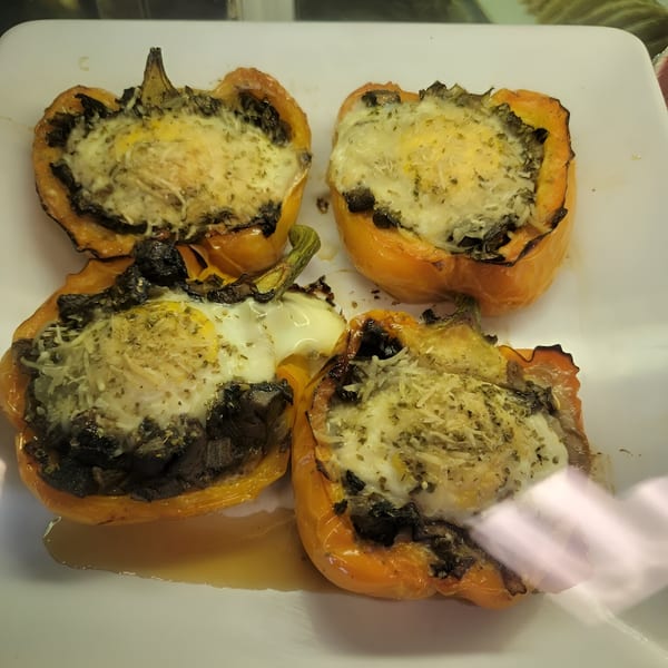 Four baked orange bell peppers stuffed with egg, cheese, and herbs on a white plate.