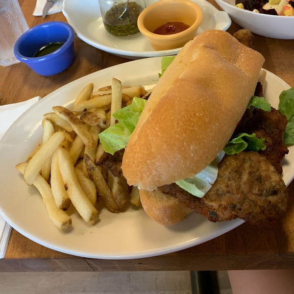 Milanesa sandwich with lettuce and a side of french fries, ketchup, and chimichurri sauce.