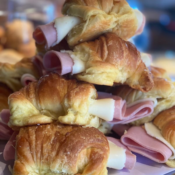 A close-up of a stack of golden-brown croissants filled with ham and cheese.