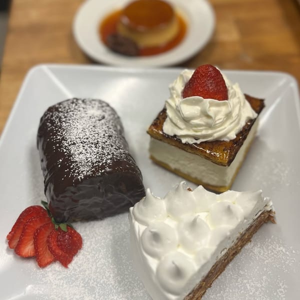 A plate of three Argentinian desserts: a chocolate roll, a strawberry cream pastry, and a meringue cake.