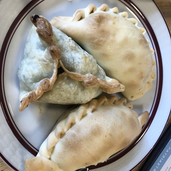 Three Argentinian empanadas, one with a decorative twisted top, on a white plate with a brown rim.