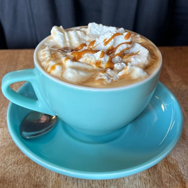 A Patria Station Café dulce de leche latte with whipped cream and caramel drizzle in a teal cup.