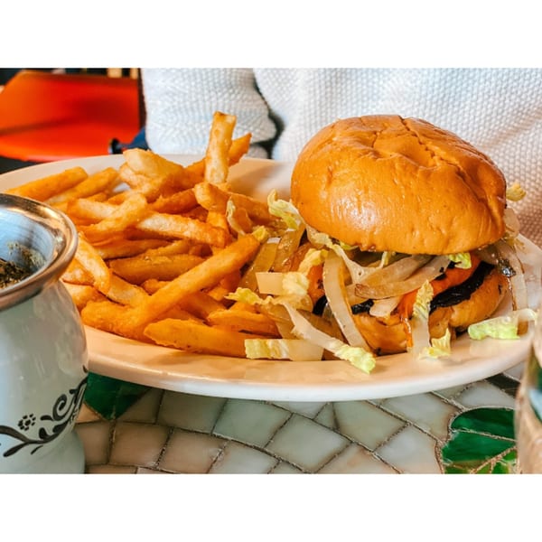 A Patria Station Café burger with lettuce, onions, and fries on a white plate.