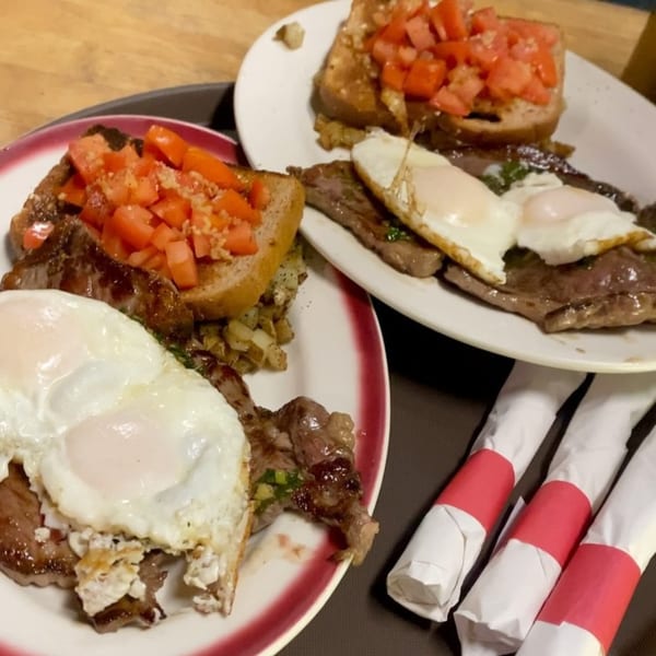 Two plates of Patria Station Café's Argentinian steak and eggs with tomato bruschetta and potatoes.